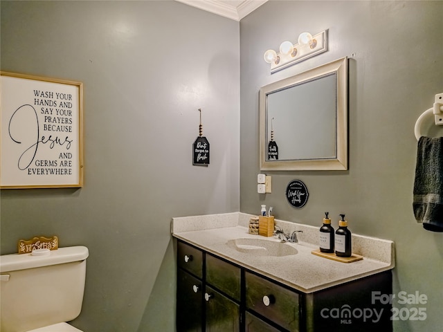 half bathroom with vanity, ornamental molding, and toilet