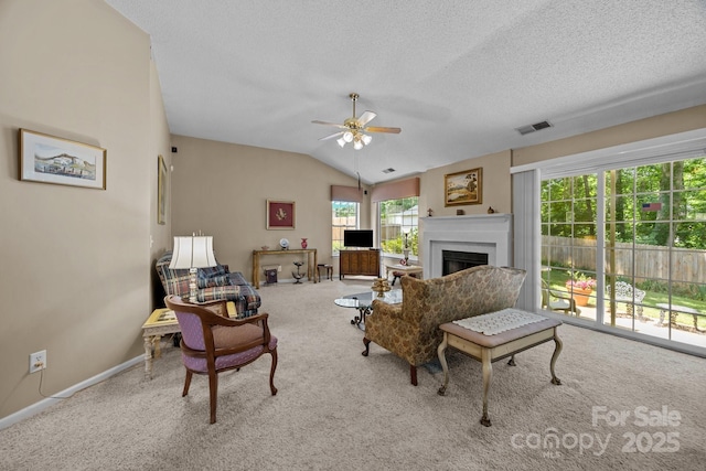 carpeted living area featuring a fireplace, ceiling fan, baseboards, a textured ceiling, and lofted ceiling