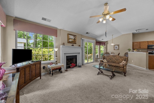 carpeted living area with healthy amount of natural light, lofted ceiling, a ceiling fan, a fireplace with flush hearth, and baseboards