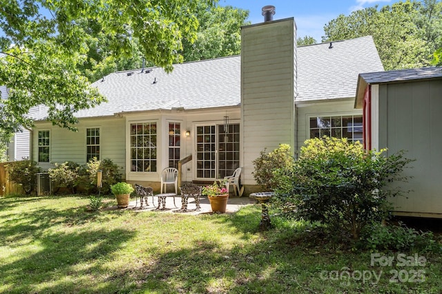 back of house with a lawn, a chimney, central AC, a shingled roof, and a patio