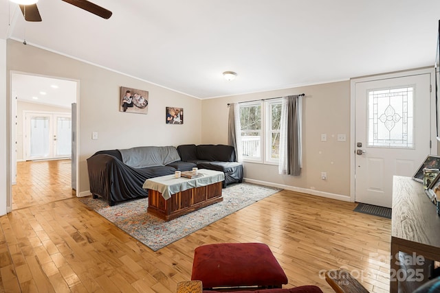 living room featuring baseboards, ceiling fan, ornamental molding, vaulted ceiling, and light wood-type flooring