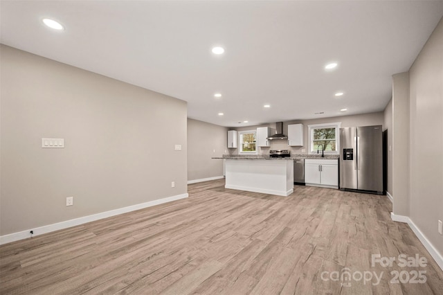 kitchen with a sink, stainless steel appliances, white cabinets, wall chimney range hood, and light wood-type flooring