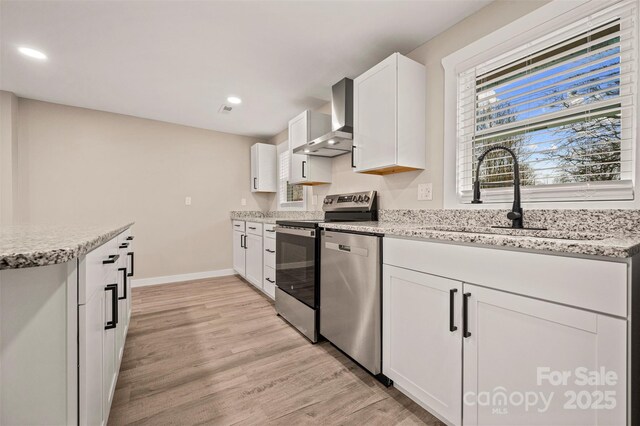 kitchen with light wood-type flooring, a sink, light stone counters, stainless steel appliances, and wall chimney range hood