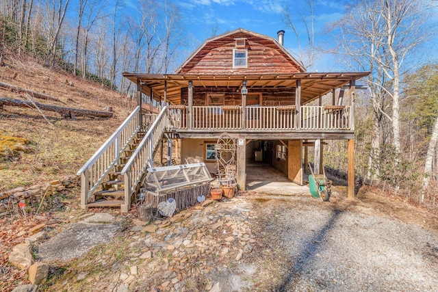 view of front of house with a gambrel roof, driveway, a carport, log exterior, and stairs