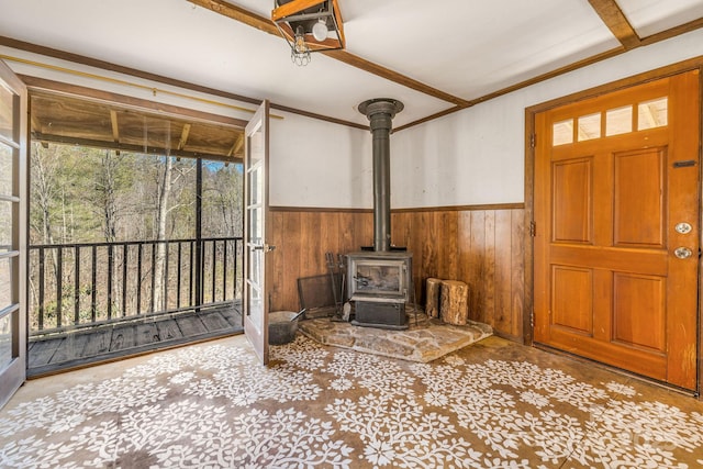 interior space featuring beam ceiling, a wood stove, wooden walls, and wainscoting