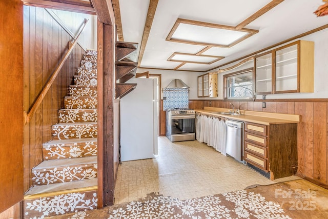 kitchen with wooden walls, glass insert cabinets, light floors, appliances with stainless steel finishes, and a sink