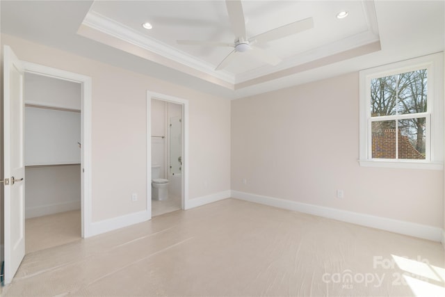 unfurnished bedroom featuring a spacious closet, crown molding, a raised ceiling, and baseboards