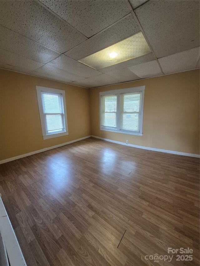 spare room featuring a drop ceiling, baseboards, and wood finished floors