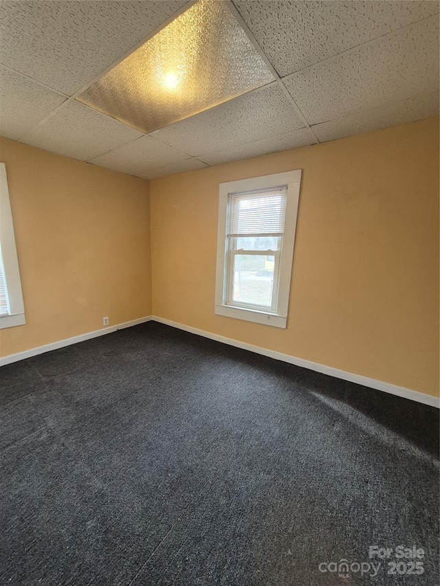 spare room featuring a paneled ceiling, carpet floors, and baseboards