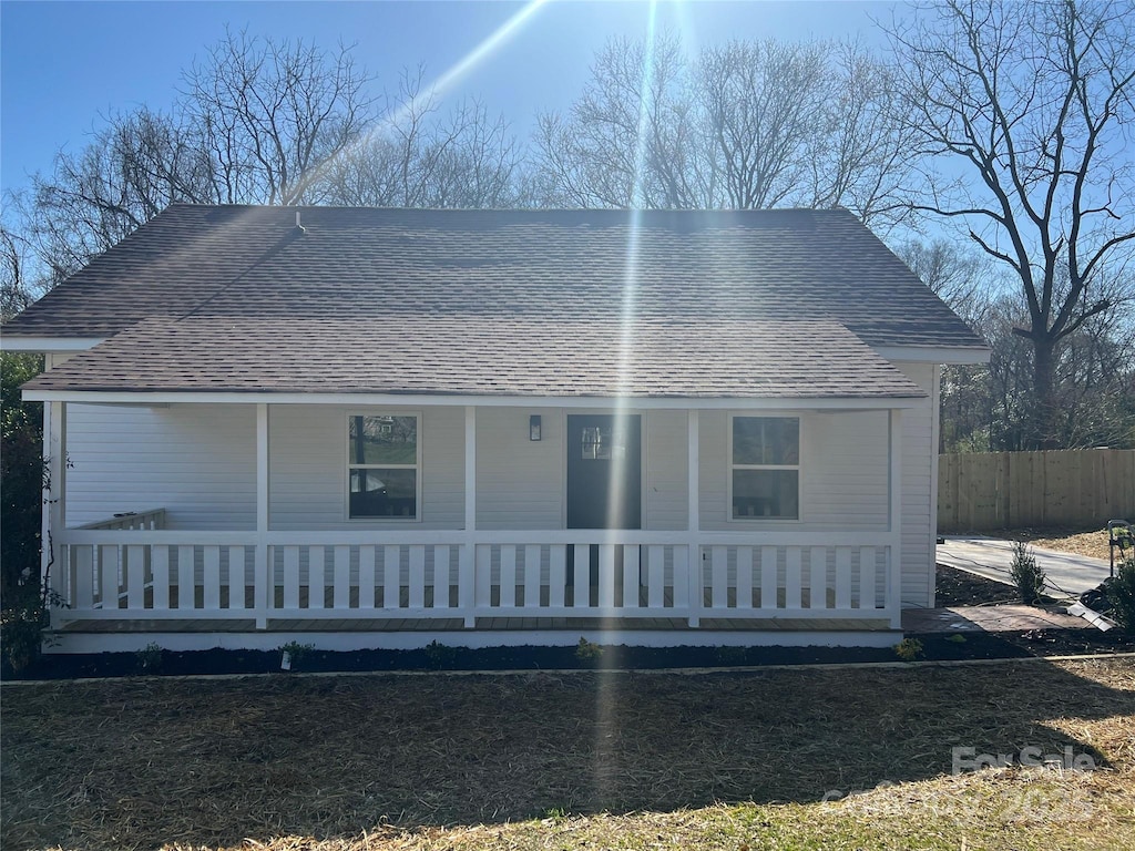 view of front facade with fence, covered porch, and roof with shingles