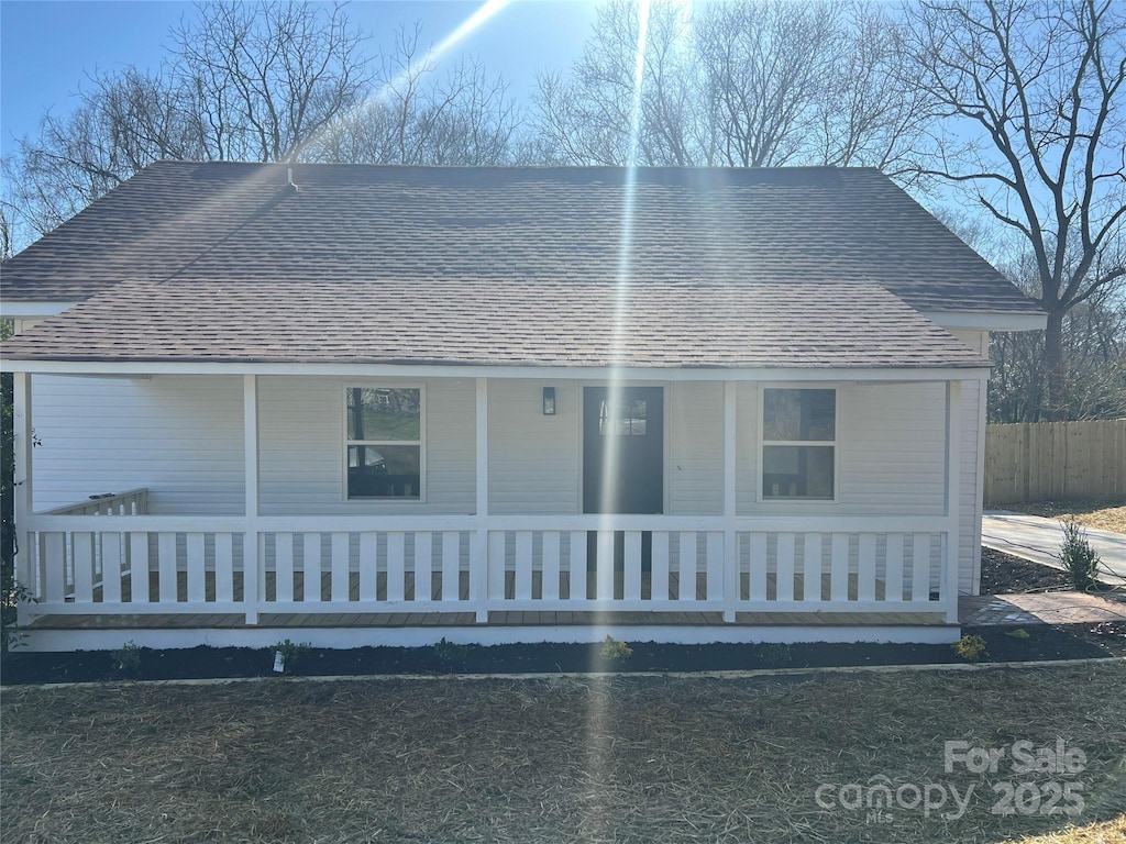 view of front of house with roof with shingles, a porch, and fence