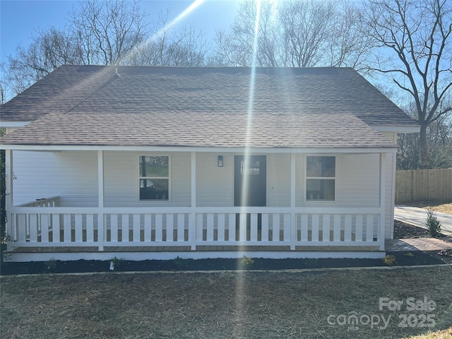 view of front of home with a porch, fence, and roof with shingles