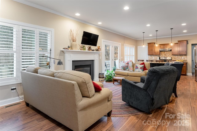 living room featuring dark wood-style floors, visible vents, recessed lighting, ornamental molding, and a glass covered fireplace