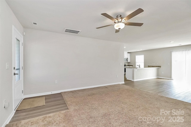 unfurnished living room with visible vents, baseboards, carpet flooring, wood finished floors, and a sink