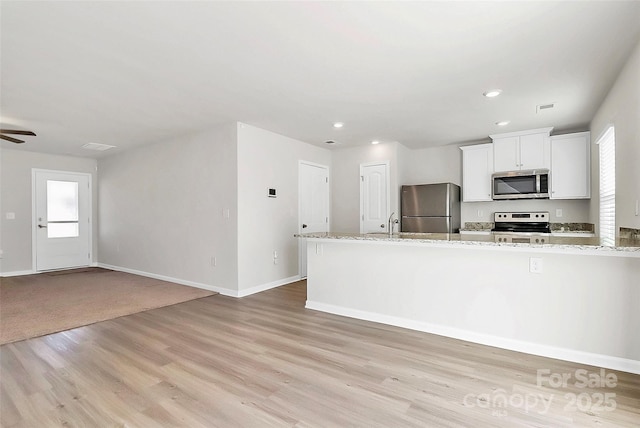 kitchen with a wealth of natural light, appliances with stainless steel finishes, light wood-type flooring, and light stone countertops