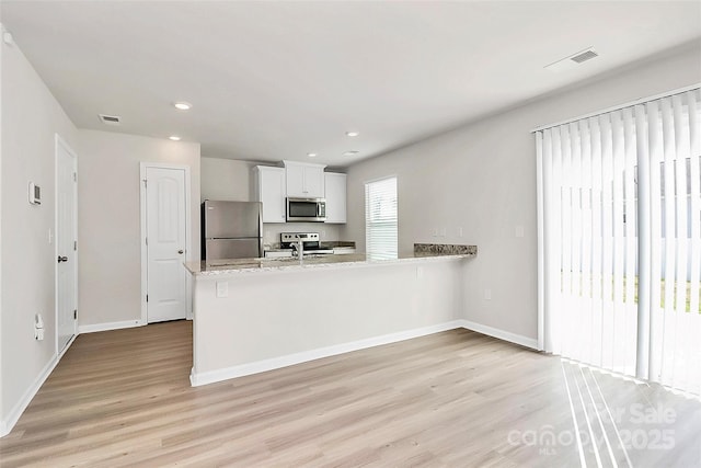 kitchen featuring stainless steel appliances, a peninsula, white cabinets, light wood finished floors, and baseboards