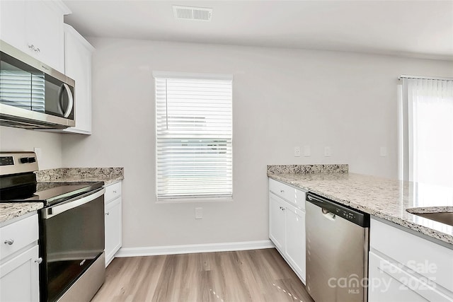 kitchen with visible vents, light stone countertops, light wood-style flooring, white cabinets, and stainless steel appliances