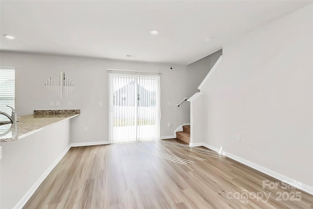 unfurnished living room featuring stairway, plenty of natural light, baseboards, and light wood-type flooring