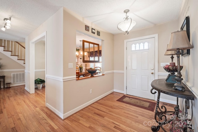 foyer entrance with visible vents, light wood-style flooring, a textured ceiling, and baseboards