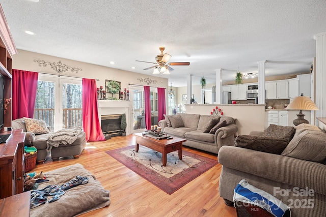 living area featuring light wood-type flooring, a textured ceiling, a glass covered fireplace, and a ceiling fan