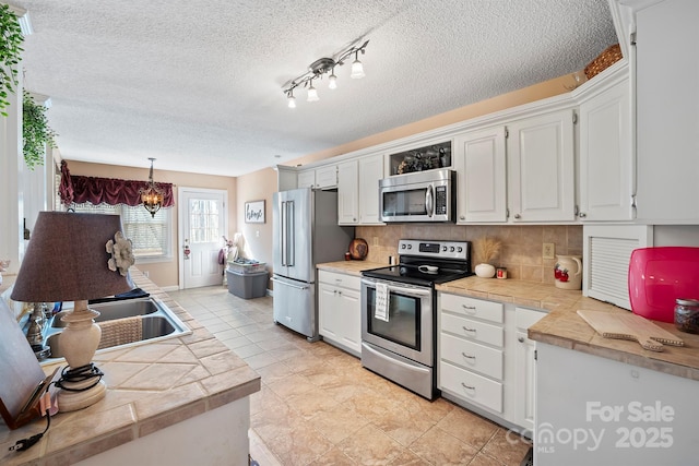 kitchen featuring a notable chandelier, a textured ceiling, appliances with stainless steel finishes, white cabinets, and decorative backsplash