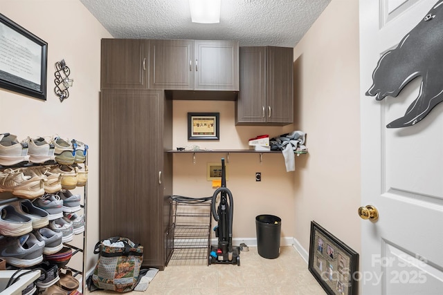 interior space featuring baseboards, hookup for a washing machine, cabinet space, hookup for an electric dryer, and a textured ceiling