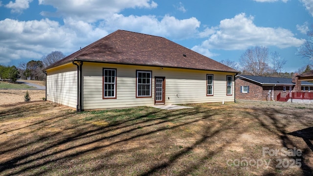 rear view of house featuring a lawn and a shingled roof