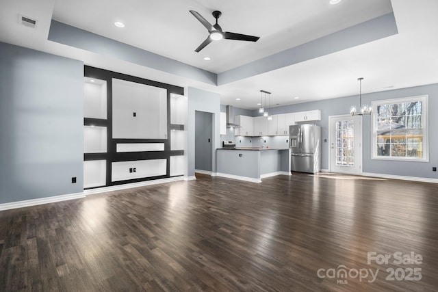 unfurnished living room with dark wood-type flooring, ceiling fan with notable chandelier, visible vents, and baseboards