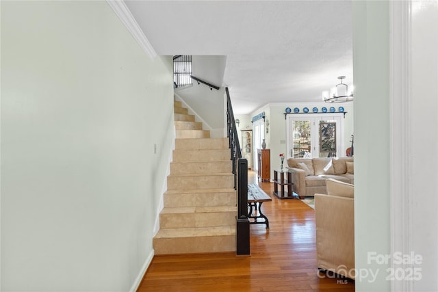 stairway with crown molding, a notable chandelier, wood finished floors, and baseboards