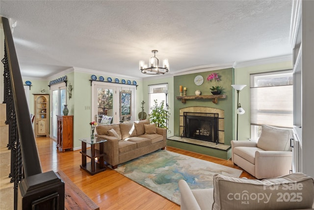 living room with a chandelier, a fireplace with raised hearth, crown molding, and wood finished floors