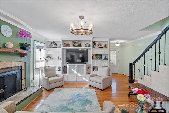 living area featuring a tiled fireplace, stairs, wood finished floors, and ornamental molding