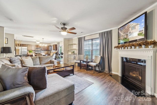 living room featuring a glass covered fireplace, baseboards, wood finished floors, and ceiling fan with notable chandelier