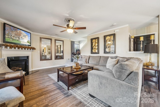 living area featuring crown molding, baseboards, ceiling fan, wood finished floors, and a glass covered fireplace