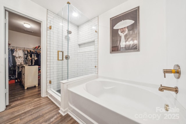 bathroom with a spacious closet, visible vents, a shower stall, wood finished floors, and a bath