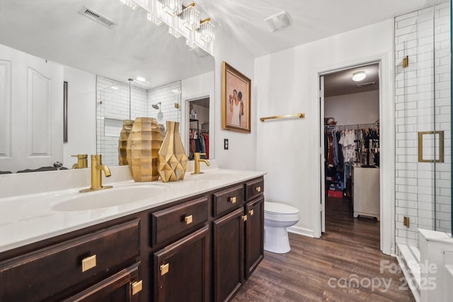 bathroom with visible vents, a shower stall, double vanity, wood finished floors, and a sink