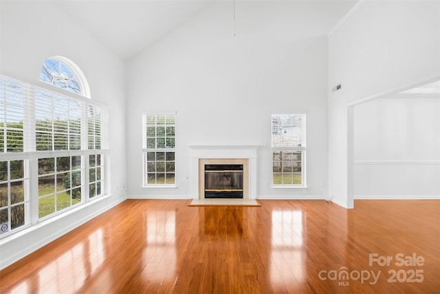 unfurnished living room with visible vents, a fireplace with flush hearth, high vaulted ceiling, wood finished floors, and baseboards