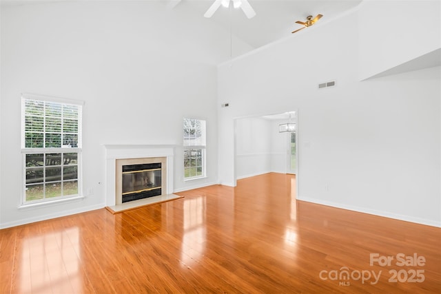 unfurnished living room featuring a high end fireplace, visible vents, wood finished floors, high vaulted ceiling, and a ceiling fan