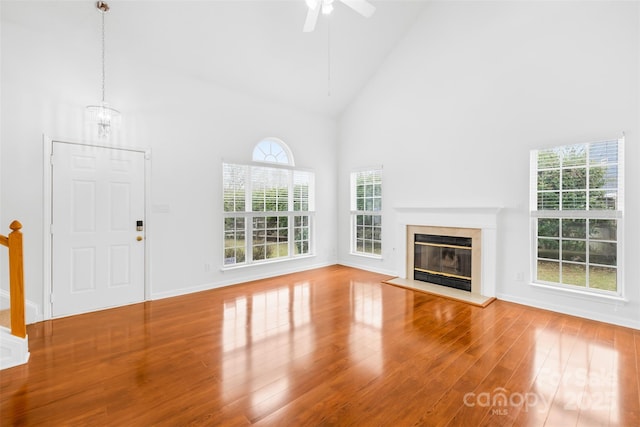 unfurnished living room with a ceiling fan, wood finished floors, baseboards, high vaulted ceiling, and a fireplace