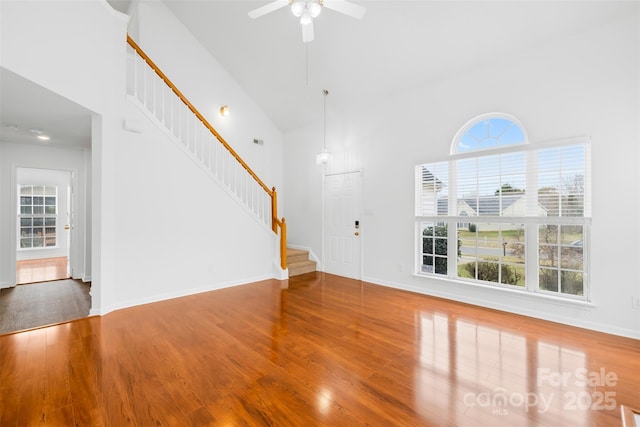 unfurnished living room with stairway, high vaulted ceiling, baseboards, and wood finished floors