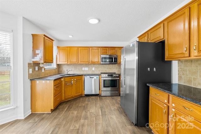 kitchen with light wood finished floors, a sink, decorative backsplash, appliances with stainless steel finishes, and brown cabinets