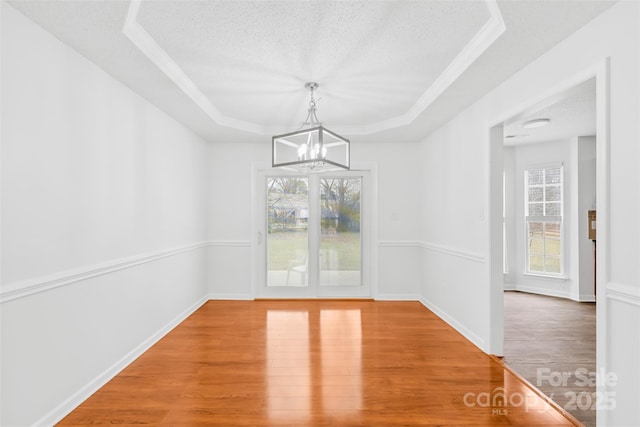 unfurnished dining area with a raised ceiling, a textured ceiling, a healthy amount of sunlight, and wood finished floors