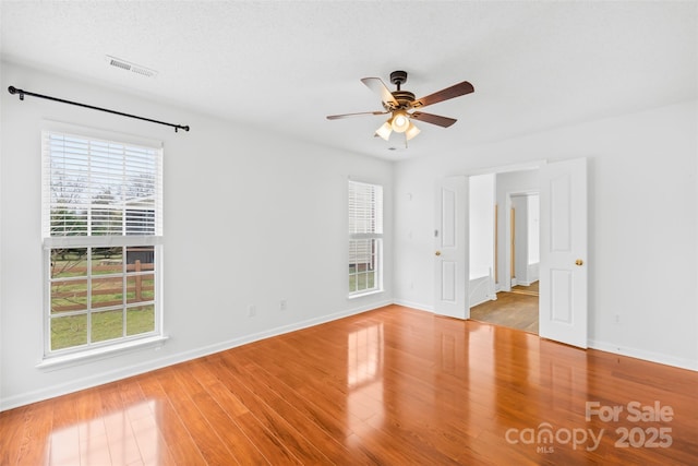 empty room with ceiling fan, visible vents, baseboards, and wood finished floors