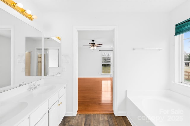 full bath featuring plenty of natural light, wood finished floors, a garden tub, and a sink