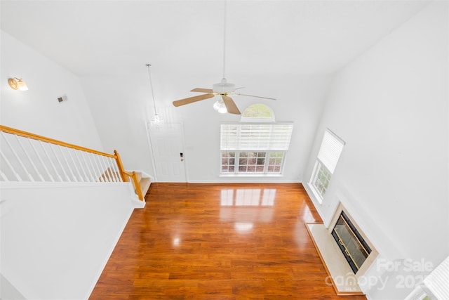 unfurnished living room with ceiling fan, a glass covered fireplace, wood finished floors, stairway, and a towering ceiling