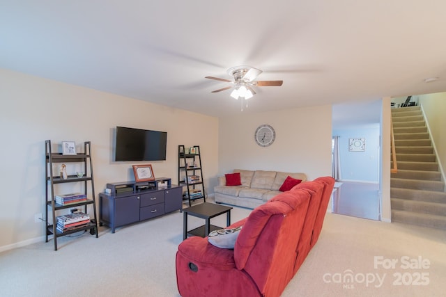 living area with baseboards, light carpet, a ceiling fan, and stairs