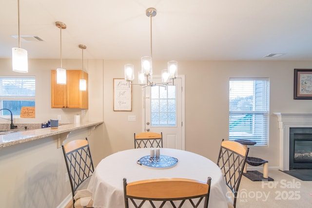 carpeted dining space with a wealth of natural light, a fireplace with flush hearth, an inviting chandelier, and a sink