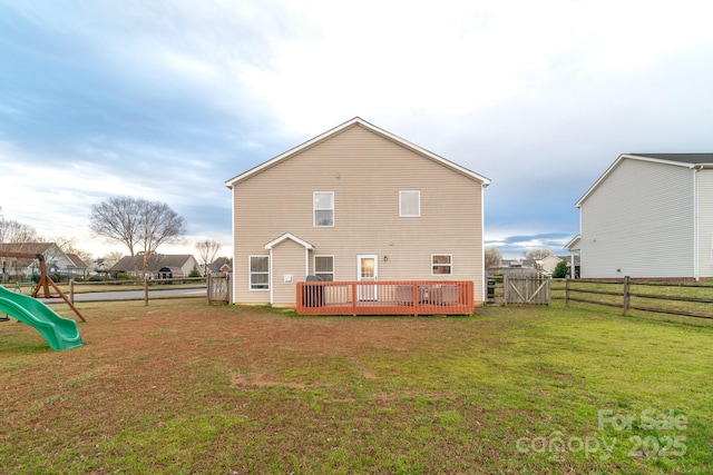 rear view of property with a deck, a playground, a yard, and fence