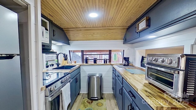 kitchen with a sink, blue cabinetry, appliances with stainless steel finishes, and wooden counters