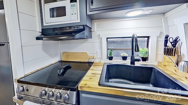 kitchen with a sink, stainless steel electric range oven, white microwave, and butcher block countertops