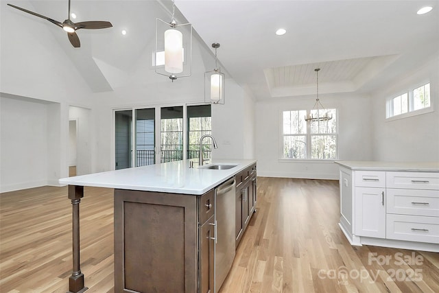 kitchen featuring light wood finished floors, dishwasher, light countertops, a tray ceiling, and a sink